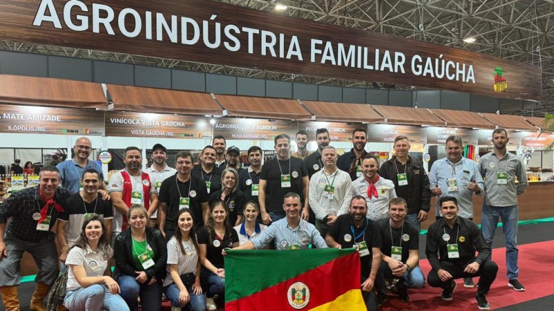 Proprietários das agroindústrias familiares posam com a bandeiro do Rio Grande do Sul em frente ao espaço destinado à agricultura familiar.