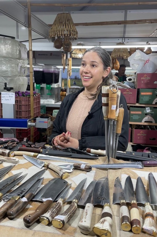 Expositora das facas coimbra, mulher branca de cabelo escuro, sorri para o cliente. No balcão, as facas estão expostas.