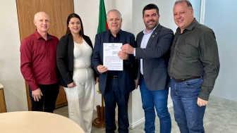 Secretário Covatti, ao centro, segura contrato da Consulta Popular. Ao seu lado esquerdo, homem de camisa vermelha e mulher de branco posam para foto. Ao seu lado direito, homem de terno e homem de camisa cinza posam para foto