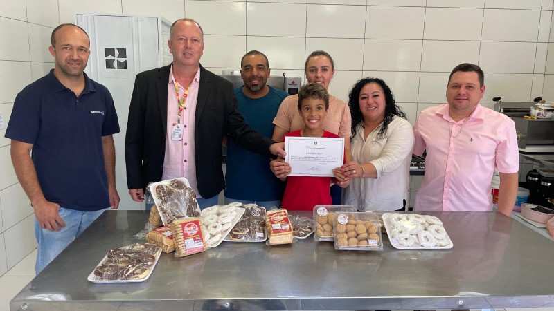 Seis adultos e uma criança posam em frente à mesa com biscoitos com o certificado de inclusão no Peaf nas mãos.